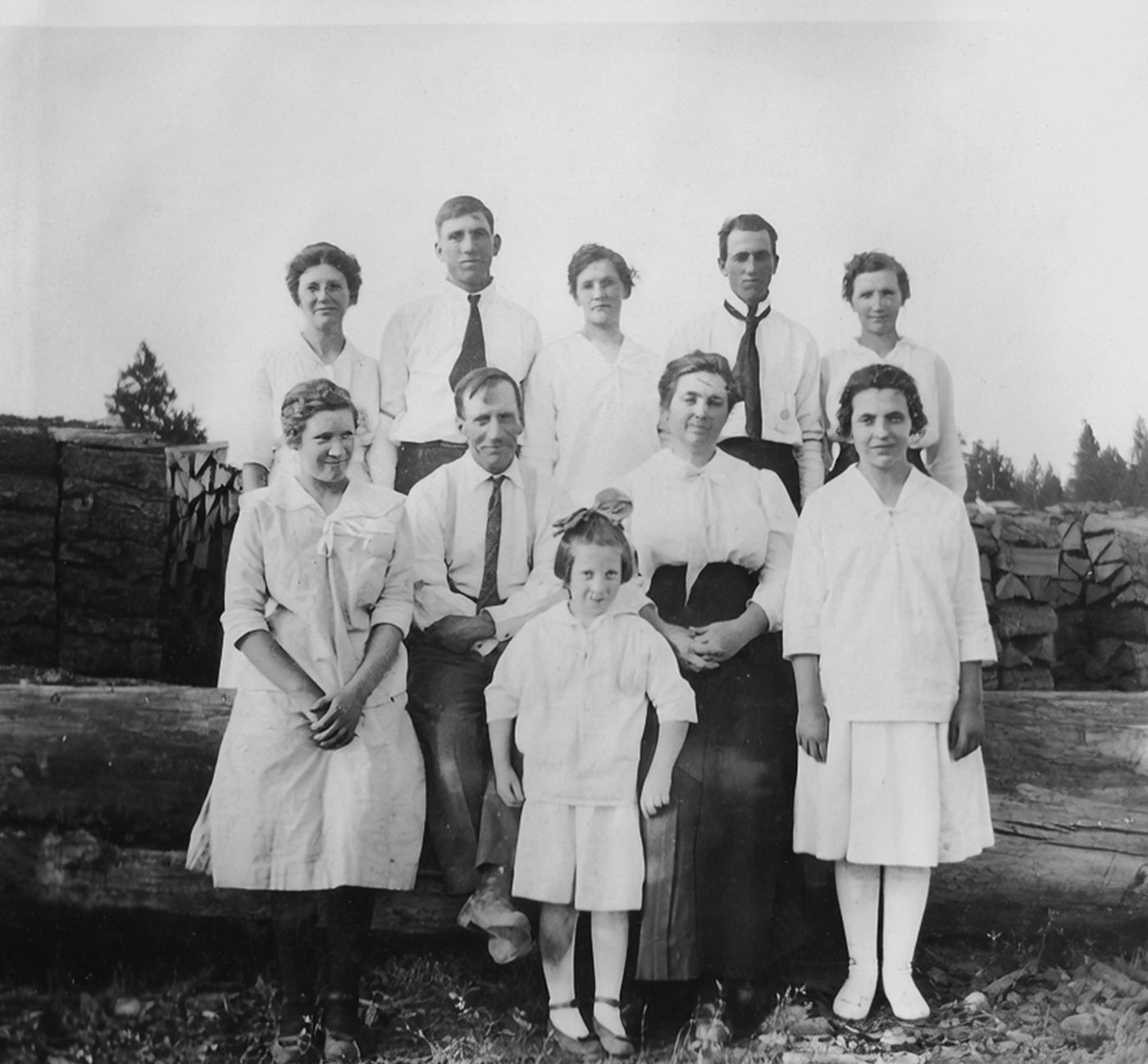 William John and Bertha Russell with their eight children, posed in two rows in front of stacked firewood, about 1916.